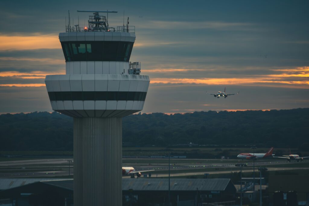 Torre de controle de tráfego aéreo ao entardecer, com um avião se aproximando para pousar ao fundo